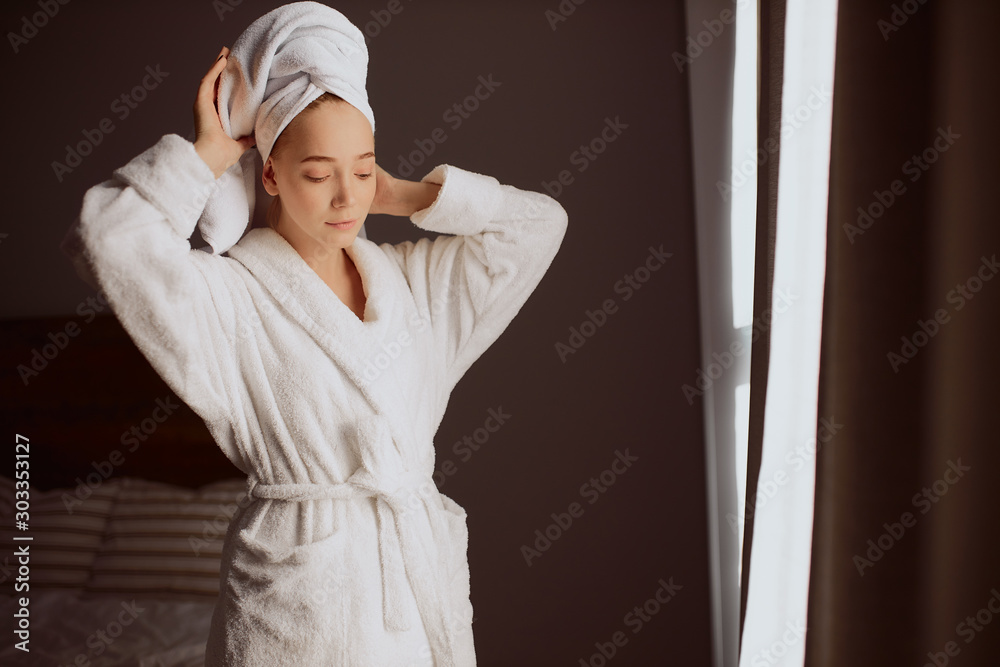 Pretty young woman raising hands, fixing towel on head, looking down with calm face, spending time at home after taking bath procedures, free time concept, portrait, indoor shot Pretty young woman raising hands, fixing towel on head, looking down with calm face, spending time at home after taking bath procedures, free time concept, portrait, indoor shot