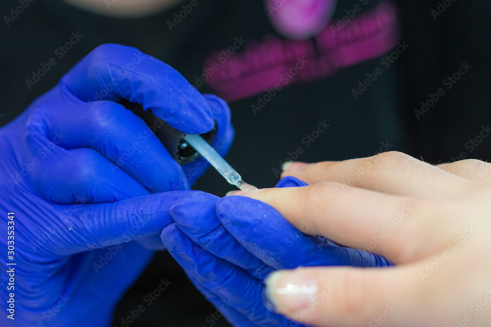 Manicurist with blue gloves polish nails on women's hand in nail salon