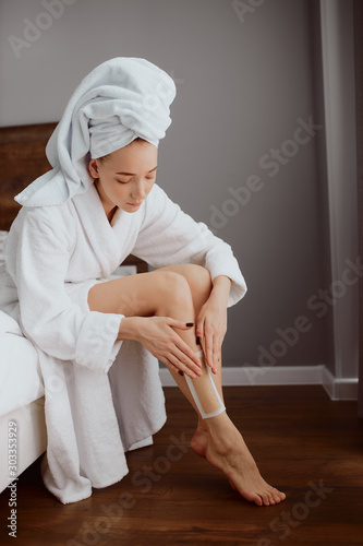 Pretty concentrated woman waxing legs sitting at home, spending time by taking care of perfect slim body, looking away, expressing calmness, involving to procedure, female beauty care, hair removal