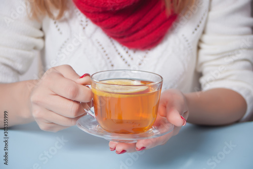 Woman's hand holding cup of tea with piece of lemon