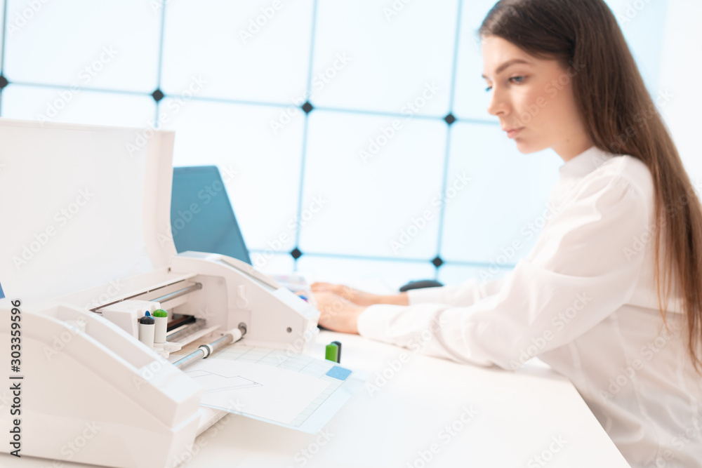 Young woman in the office of the printing company sets up a plotter for printing advertising brochures Young woman in the office of the printing company sets up a plotter for printing advertising brochures