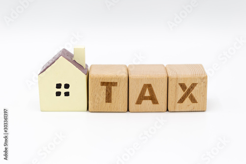 Tax letter on wooden block with coins stack, shopping cart and home model on white background.