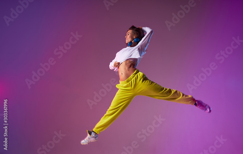 Fototapeta Naklejka Na Ścianę i Meble -  Charming young lady jumping high making acrobatics movies in the air, performing dancing skills, isolated on bright coloured background, urban lifestyle concept