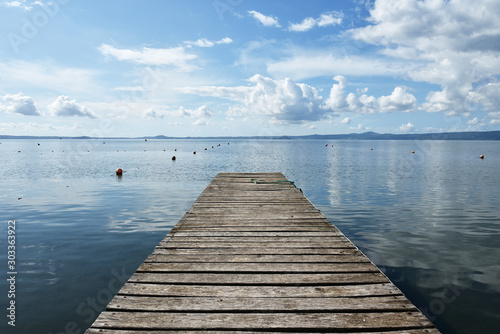 Wooden jetty for boats against a blue sky with some clouds. Floating buoys. Hills on background. Bolsena lake  Italy.