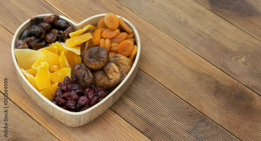 Dried fruits mix baner in wooden heart shape box isolated on wooden background. Top view of various dried fruits figs, apricots, mango, cranberries. Copy space. Dried fruits mix baner in wooden heart shape box isolated on wooden background. Top view of various dried fruits figs, apricots, mango, cranberries. Copy space.