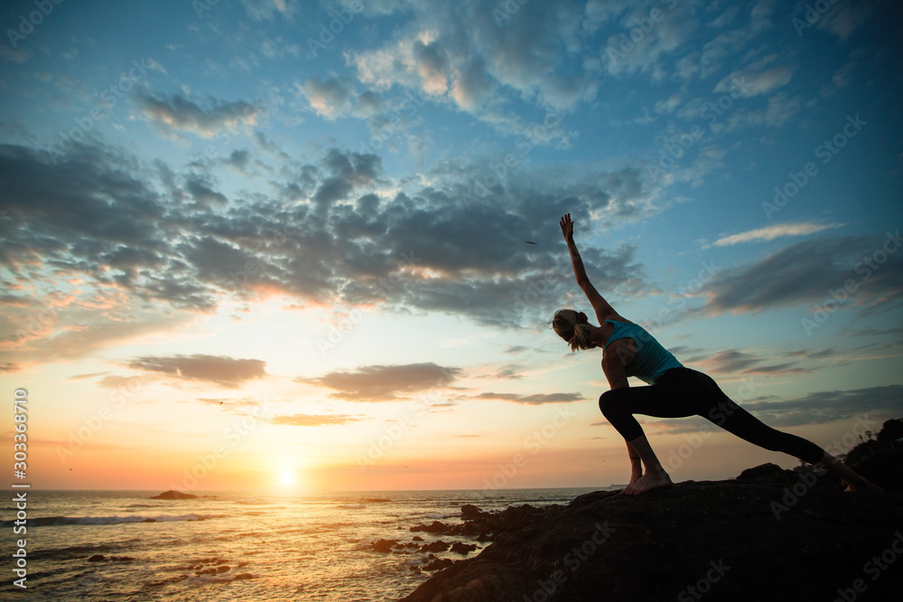 Yoga woman doing exercise on the ocean coast during a sunset.