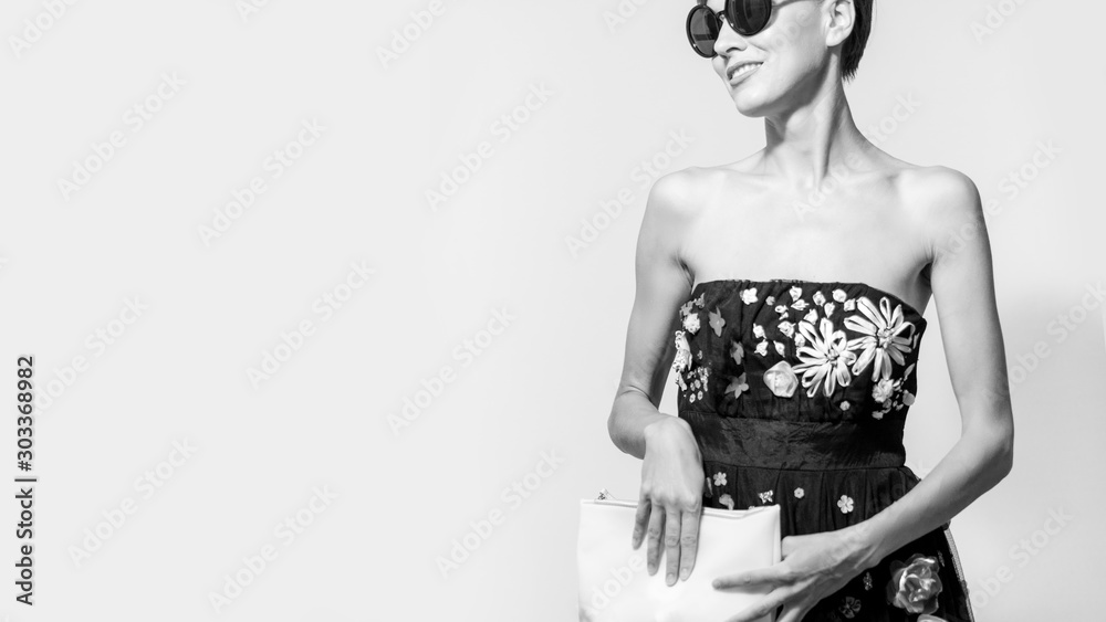  portrait of stylish brunette woman in black sexy dress, holding hand bag and wearing sunglasses - obrazy, fototapety, plakaty 