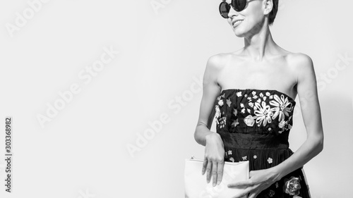  portrait of stylish brunette woman in black sexy dress, holding hand bag and wearing sunglasses