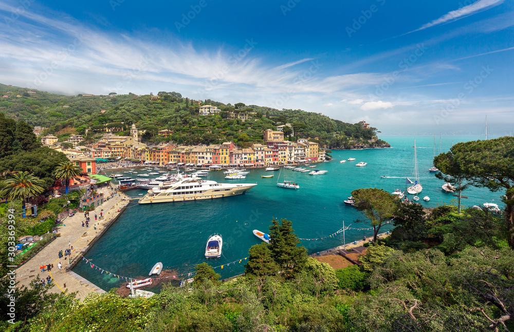 Portofino, Italian Riviera, Liguria, Italy - Panorama of the colorful coastal village with beautiful sky and multicolored houses, villas, luxury yachts and fishing boats in the turquoise harbor bay