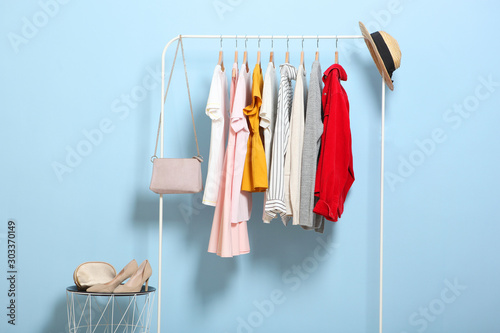 fashionable clothes on hangers on a wardrobe rack on a colored background.