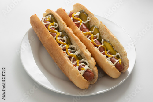 Homemade hot dogs with sausages and pickled cucubers in plate, isolated. White background. photo