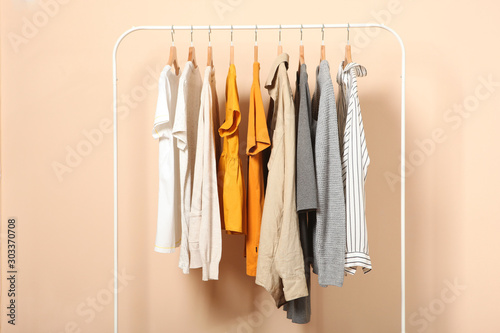 fashionable clothes on hangers on a wardrobe rack on a colored background.