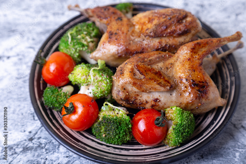Quail fried whole with broccoli and cherry tomatoes. Black plate, marble background. Selective focus, close up. Quail fried whole with broccoli and cherry tomatoes. Black plate, marble background. Selective focus, close up.