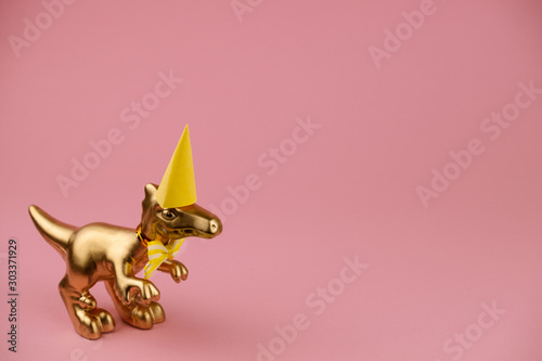golden dinosaur in a perty hat and bowtie on a pink background with copy space photo