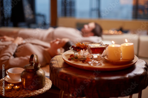 young caucasian man and woman wearing bathrobe, lying down and relxing at spa in beauty salon.Closeup photo of tea and candles while couple lying behind. Relax and healthy lifestyle concept photo