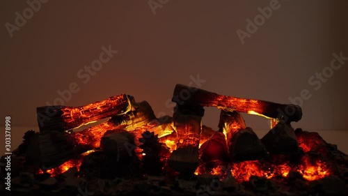 There are some glowing and burning charry logs in a fireplace in a dark room.