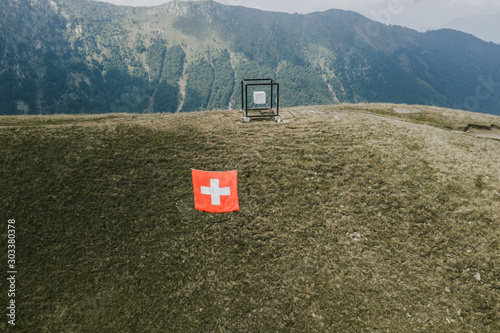 Ticino, Switzerland - August 5, 2019: Suspened cube by Jaya Schurch and siwss flag on Monte Tamaro photo