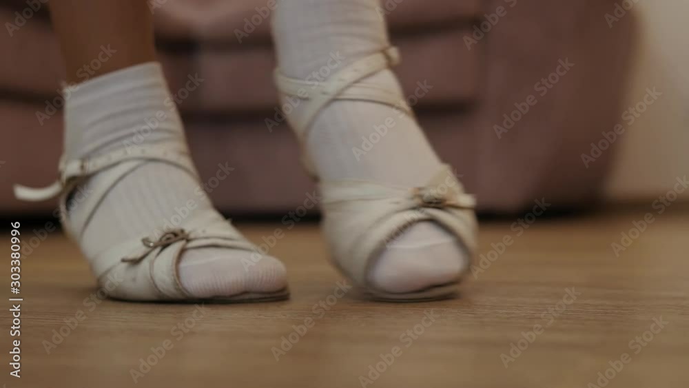 There are the feet of a girl taking dancing steps in a big living-room along the sofa. She is wearing white socks and sandals and moving like a ballerina. A great concept for a dance school. There are the feet of a girl taking dancing steps in a big living-room along the sofa. She is wearing white socks and sandals and moving like a ballerina. A great concept for a dance school.