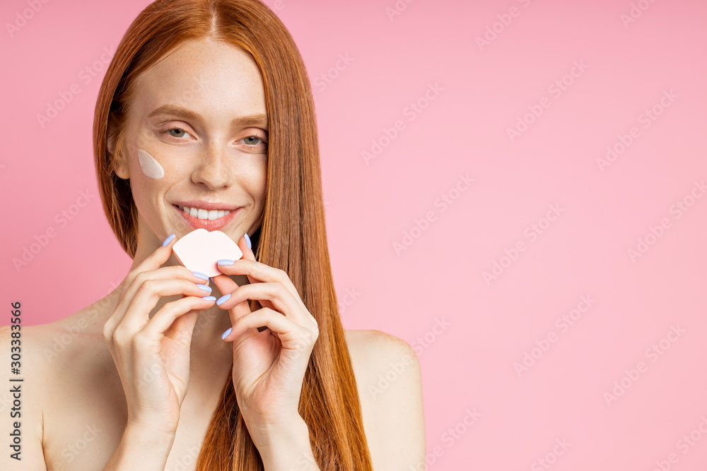Portrait of young woman applying face cream and cleansing face with sponge Portrait of young woman applying face cream and cleansing face with sponge