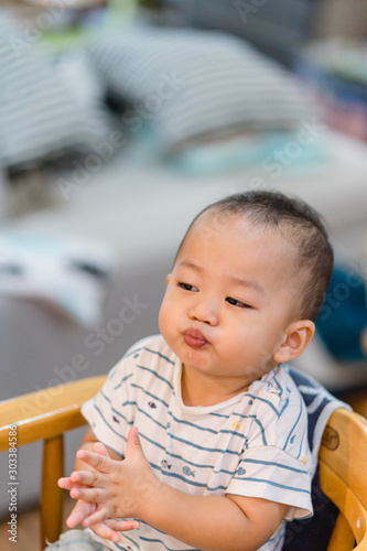Portrait of adorable baby boy with funny hungry face sitting on table in restaurant while waiting for food.