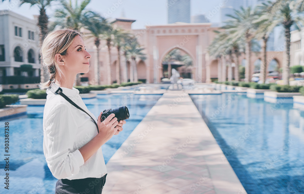 Enjoying travel in United Arabian Emirates. Happy young woman with camera taking photo in Dubai Downtown.