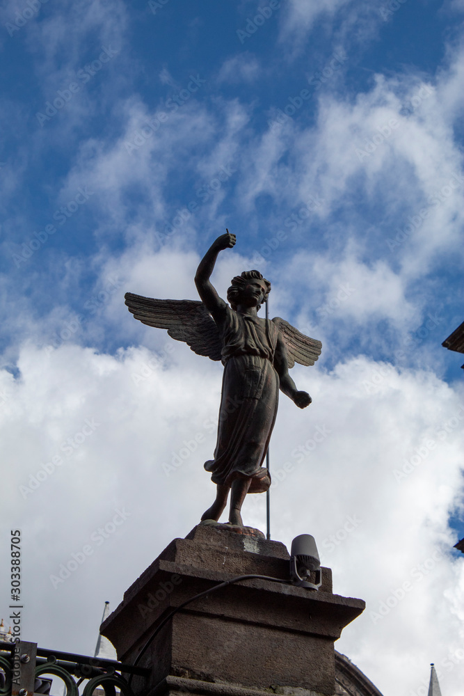 Ángel guardián de bronce con fondo azul y nubes