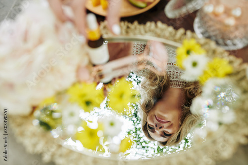 Reflection of young smiling blond woman in selver tray with daisy flowers and cosmetics
