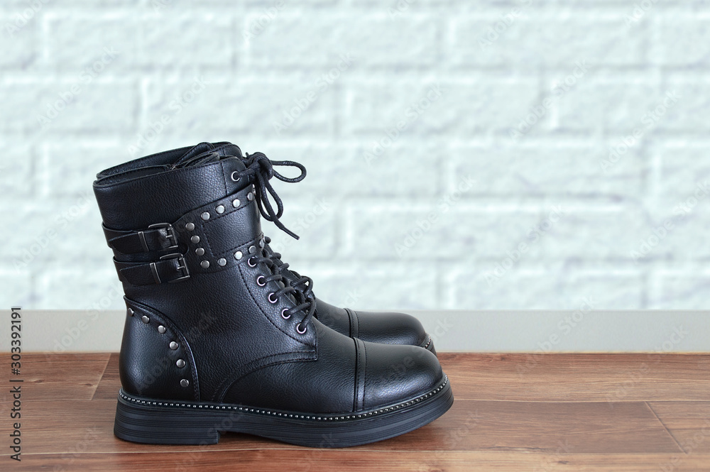 Close-up of black biker boots with metal fittings on a background of a brick white wall. Close-up of black biker boots with metal fittings on a background of a brick white wall.