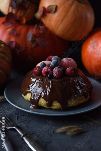 Thanksgiving hygge dessert. Homemade pumpkin pudding with chocolate icing and frozen berries and bright orange winter squashes on dark background