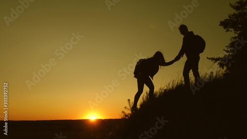 male traveler holds the hand of a female traveler helping to climb top of the hill. Tourists climb the mountain at sunset  holding hands. team work of business partners. Happy family on vacation.