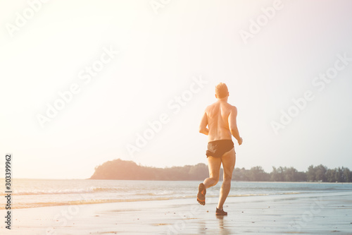 Fototapeta Naklejka Na Ścianę i Meble -  Man running on the beach in Sunset time.Summer paradise beach of Phuket island.Cardio, runner, running in Marathon concept.