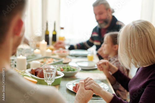 Young man  his mature mother and the rest of family holding by hands by table
