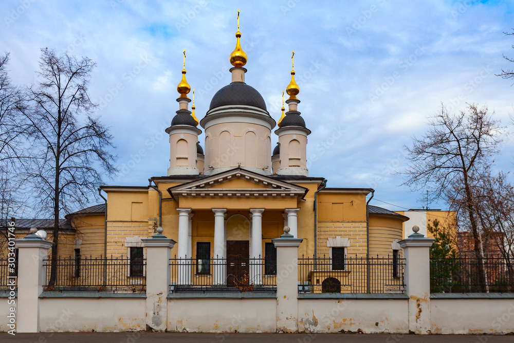 Orthodox church of yellow color with golden domes and white columns against a cloudy sky