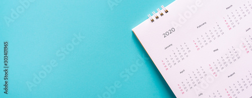 close up top view on white calendar 2020  month schedule to make appointment meeting or manage timetable each day lay on blue background for planning work and life concept photo