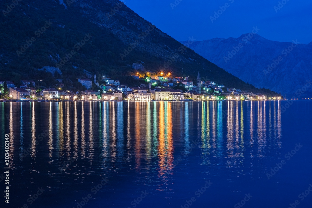 Lights of the ancient town of Perast (Montenegro) at night, reflecting on water. Bay of Kotor at blue hour. Cityscape at night, background.