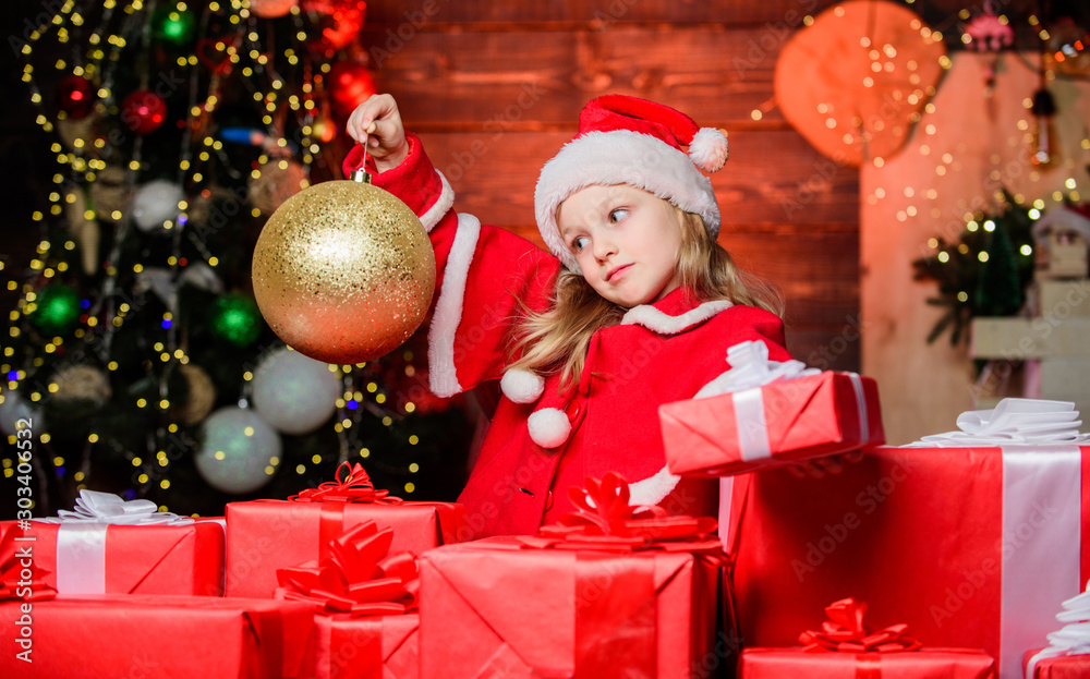 Magic glass ball makes her feel the unique atmosphere of Christmas. Small child holding christmas glitter ball. Little girl looking at ornament ball. Cute kid with golden christmas ball Magic glass ball makes her feel the unique atmosphere of Christmas. Small child holding christmas glitter ball. Little girl looking at ornament ball. Cute kid with golden christmas ball