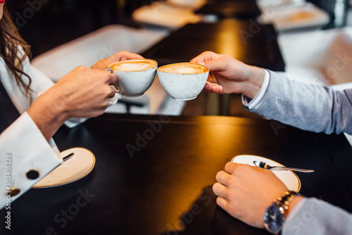 Εκτύπωση καμβά Close up image of man and woman clink coffee mugs with latte in cafe