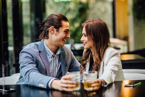 Lovely concept  pretty young and cheerful couple with drinks on hands spend time at restaurant.