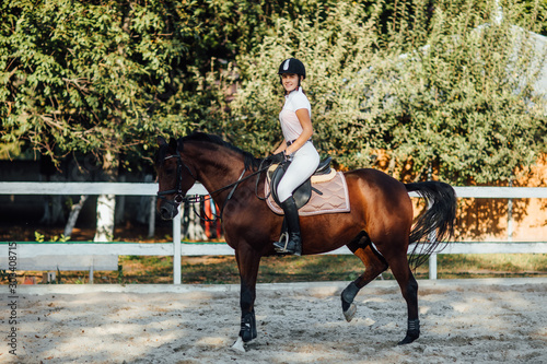 Equestrian sport event at fall with copy space. Young woman riding bay horse on dressage advanced test.