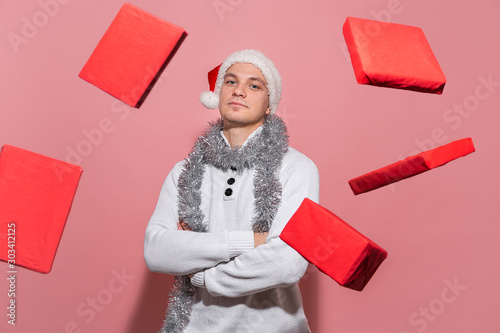 Handsome man in a white sweater, Santa hat and trumpery shows magic Christmas gifts levitating around him. photo