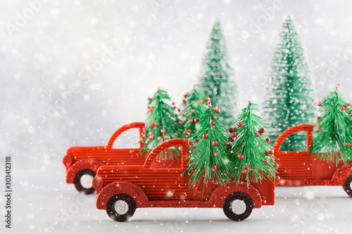 Small toy cars carring christmas tree on blue background with snow . Sesonal holidays, greeting card, christmas mood concept.
