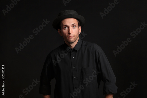 Stylish handsome man a black shirt and pork pie hat isolated over black background. Low key portrait.