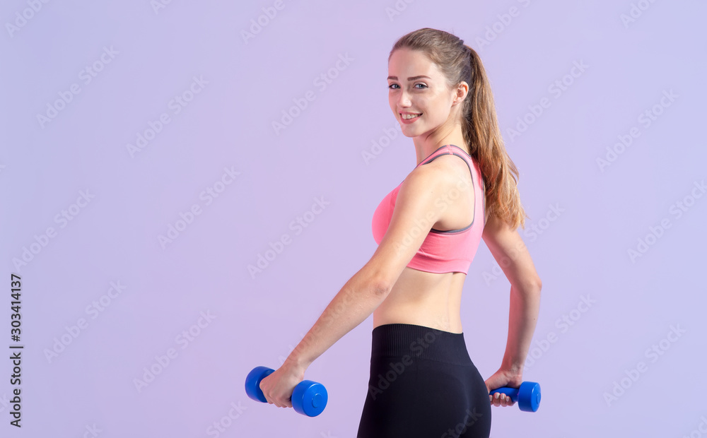 Young woman with dumbbells in hands on purple background. Happy girl is engaged in fitness. Young woman with dumbbells in hands on purple background. Happy girl is engaged in fitness.