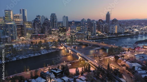 Aerial: Hyperlapse timelapse establishing shot of the Calgary city skyline at night. In the foreground is the Peace Bridge & the Bow River