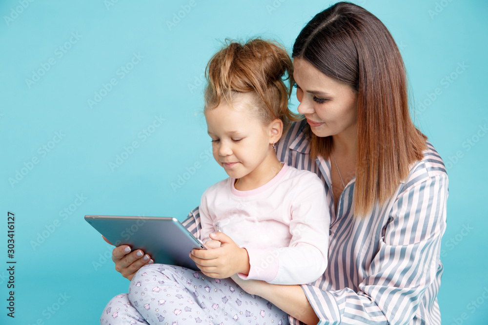 Portrait of mother and daughter with tablet sitting on the floor isolated over the blue studio Portrait of mother and daughter with tablet sitting on the floor isolated over the blue studio