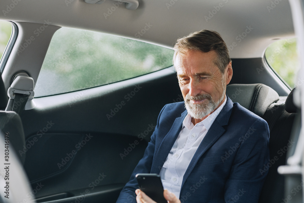 Businessman sitting in the car using a smartphone. Man checking cell phone on a backseat.