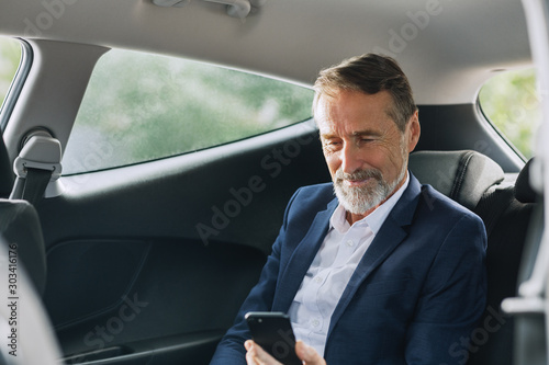Businessman sitting in the car using a smartphone. Man checking cell phone on a backseat. © Artem Varnitsin