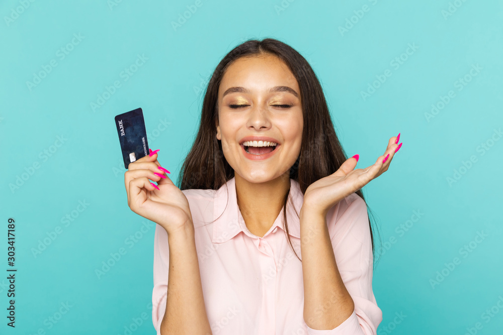 Glad and happy female person holding credit card standing on the blue background Glad and happy female person holding credit card standing on the blue background
