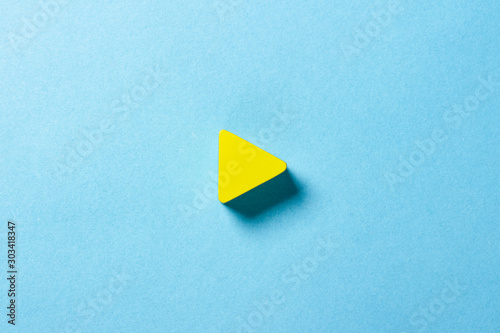 Yellow triangle on a blue background. Play sign. Minimalism. Flat lay, top view