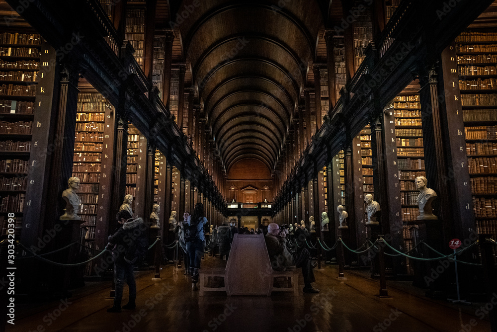 Fototapeta premium DUBLIN, IRLANDIA, 21 grudnia 2018: Długi pokój w bibliotece Trinity College, gdzie znajduje się Księga z Kells. Widok perspektywiczny miejsca z dużą ilością książek i posągów na skrzyni.